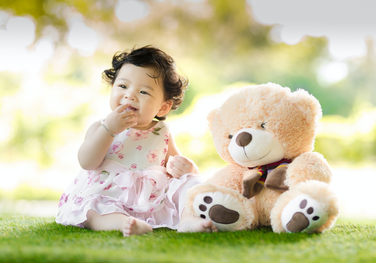 baby-sitting-on-green-grass-beside-bear-plush-toy-at-daytime-1166473
